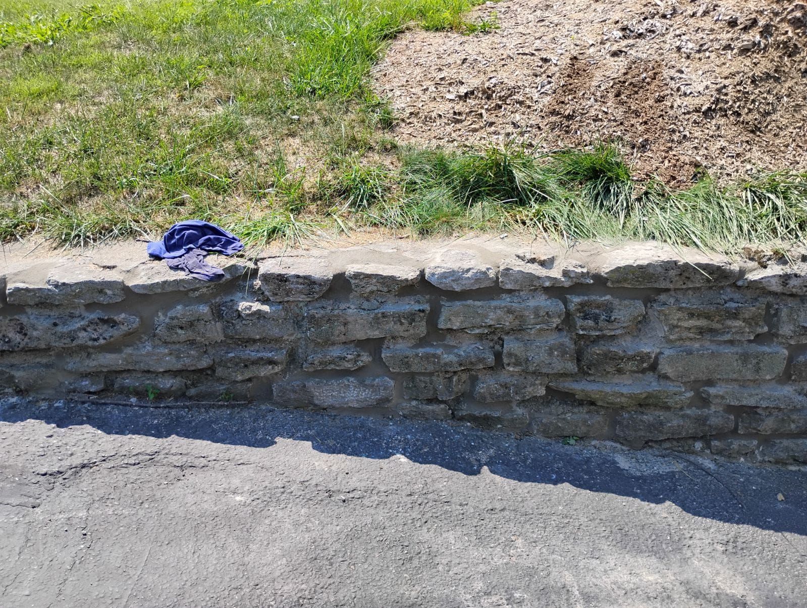 A stone wall is being built next to a grassy field.