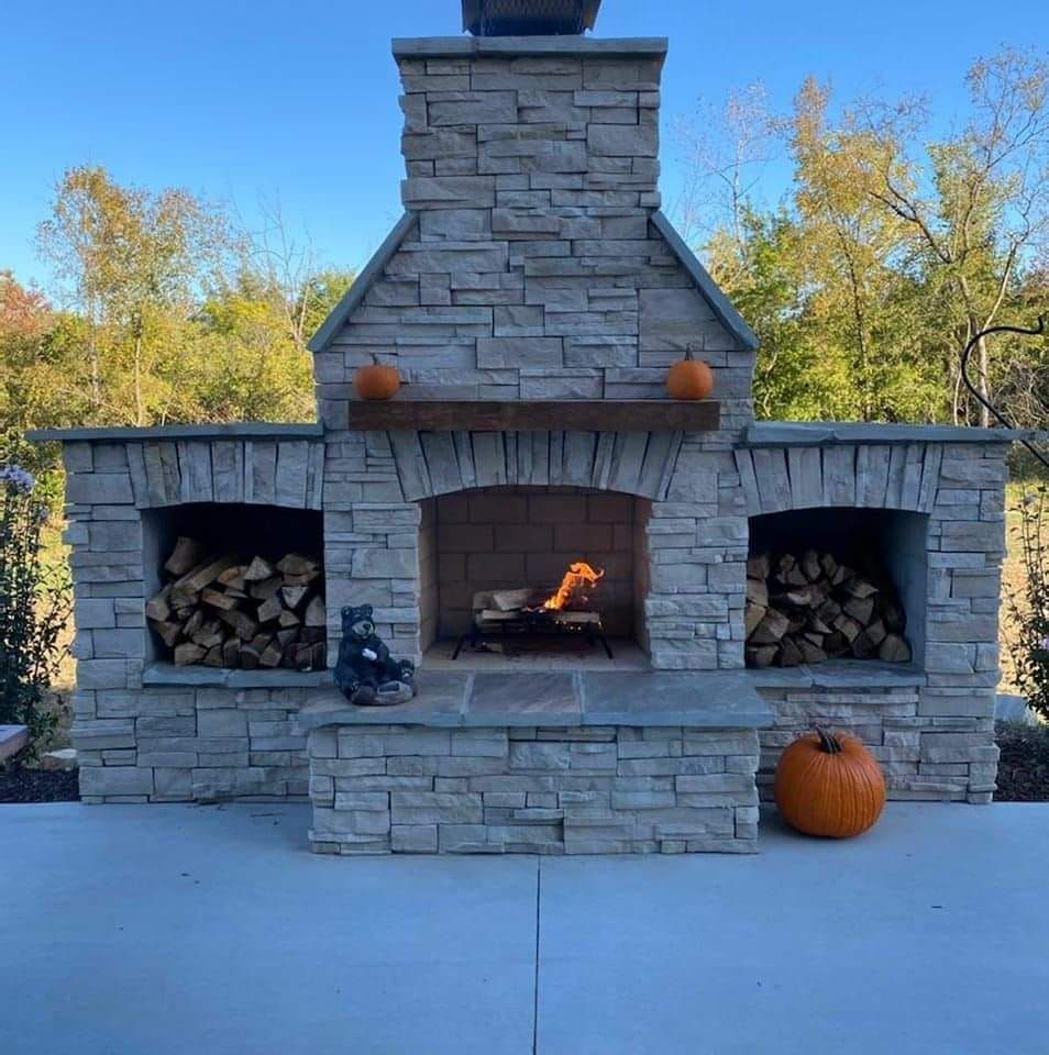 A stone fireplace with pumpkins and a bear statue in front of it.