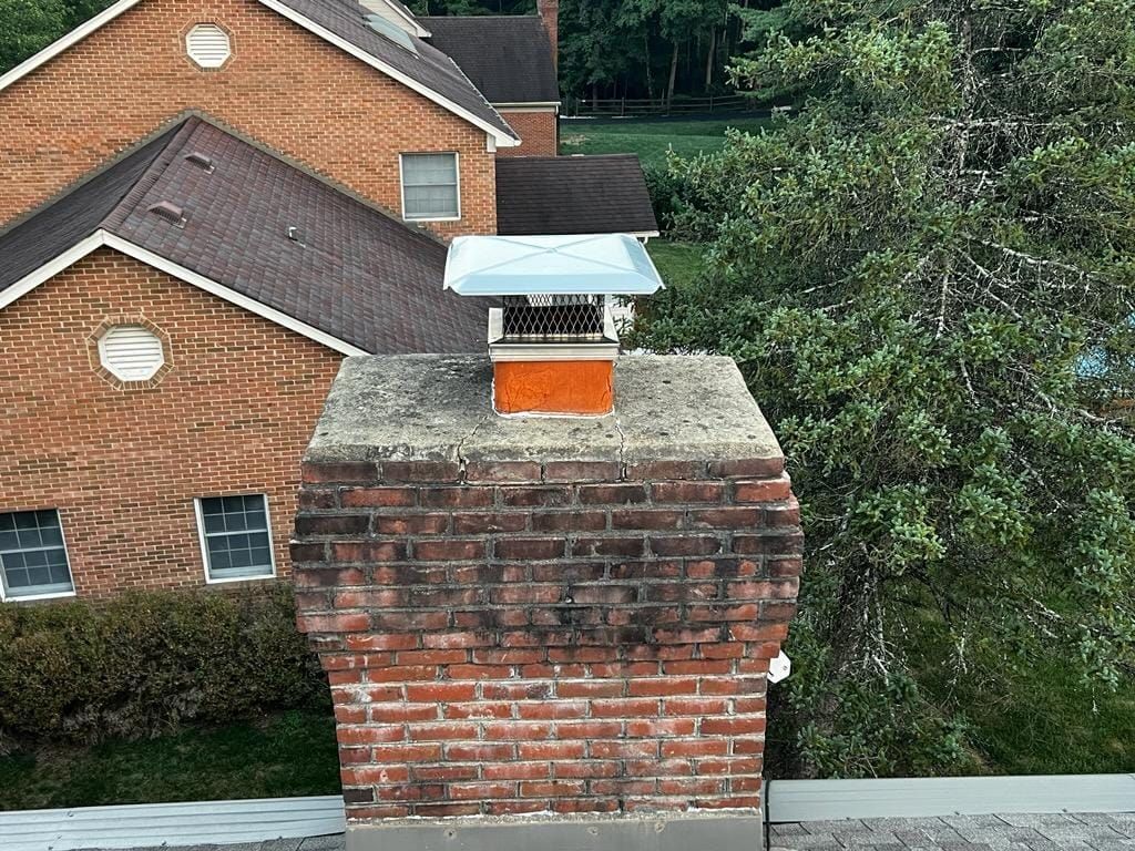 A brick chimney on top of a roof in front of a brick house.