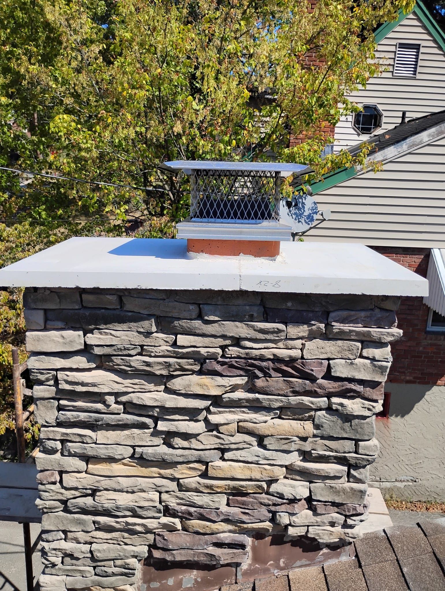 A chimney is sitting on top of a stone wall next to a roof.