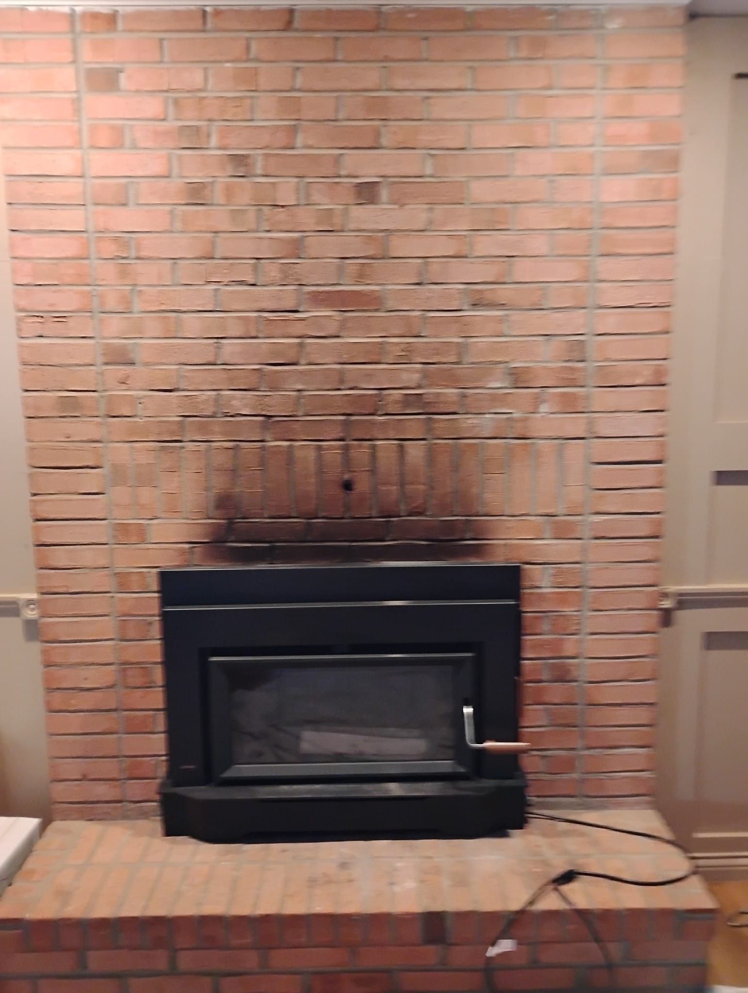 A brick fireplace with a black fireplace insert in a living room.