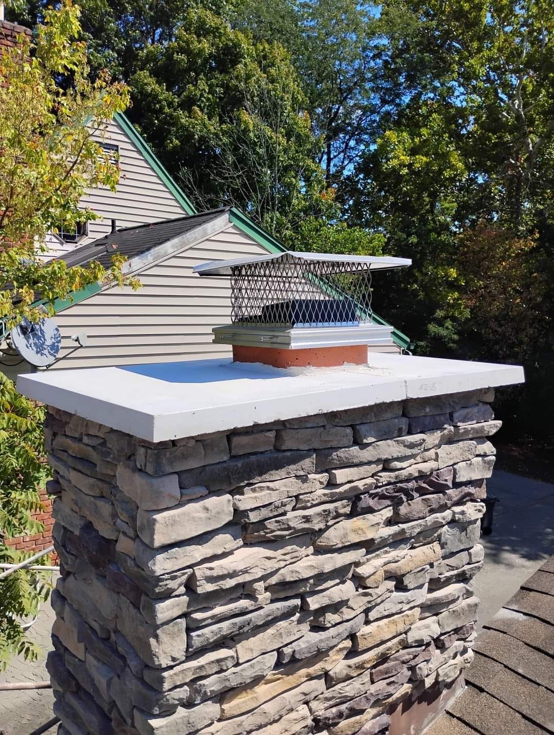 A stone chimney sitting on top of a roof next to a house.