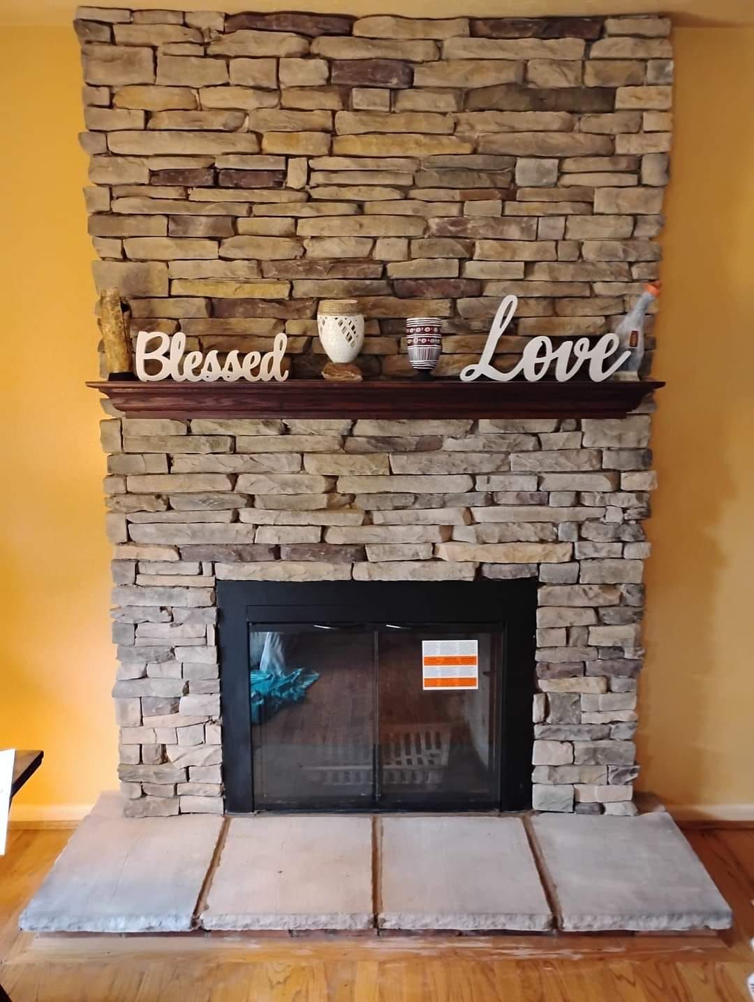 A stone fireplace with a sign on the mantle that says blessed love.