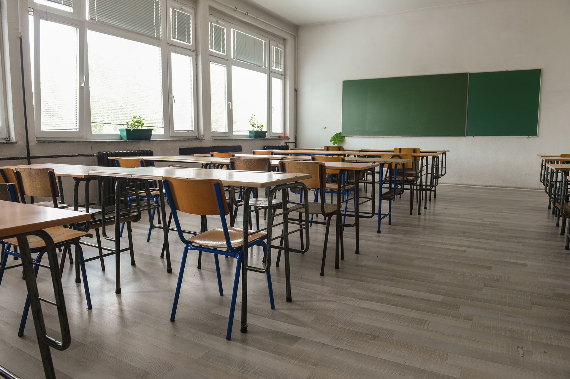 An empty classroom with tables and chairs and a green board.