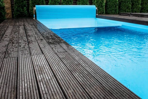 Modern blue swimming pool featuring an automatic retractable pool cover rolling over a dark wood deck.