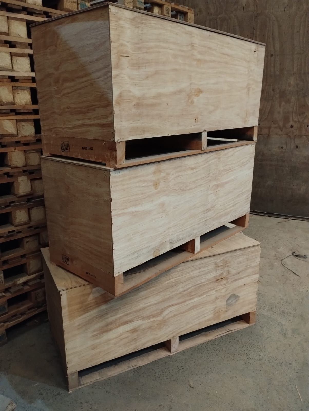 Tres cajas de madera apiladas sobre paletas, dentro de un almacén.