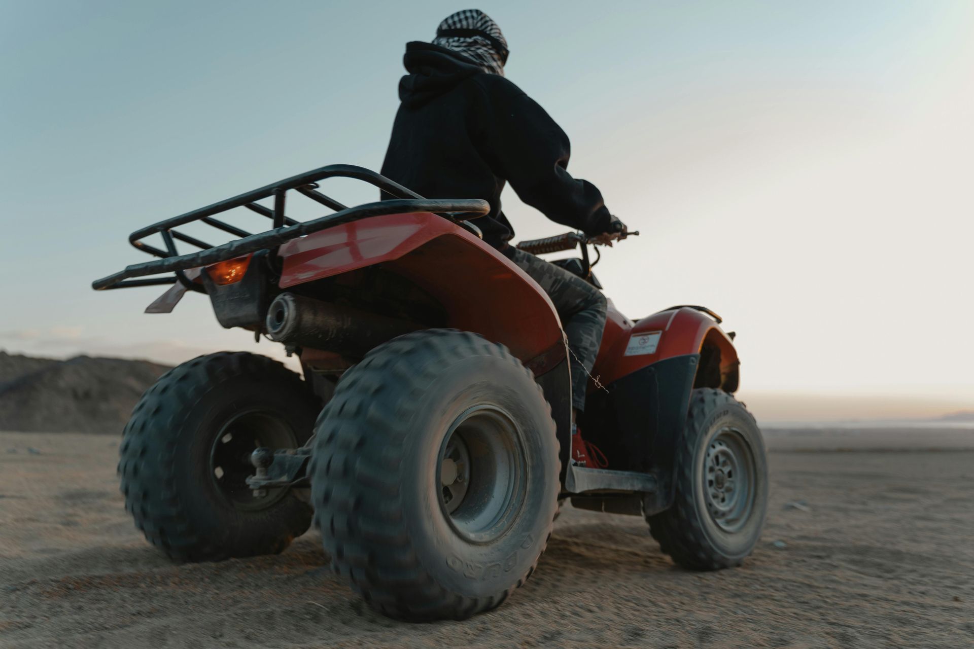 A man is riding a red atv in the desert.