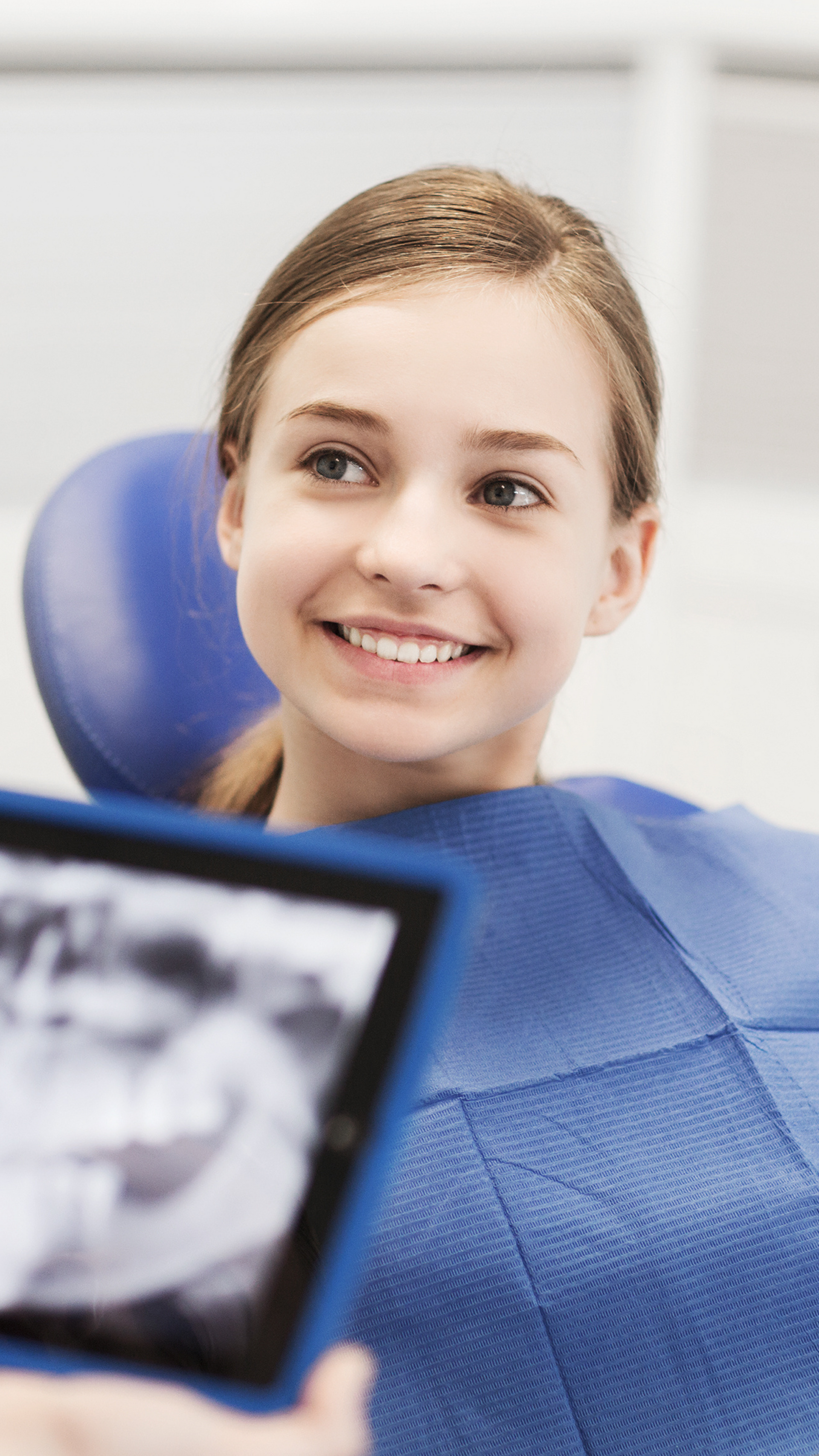 A young girl is sitting in a dental chair looking at an x-ray.