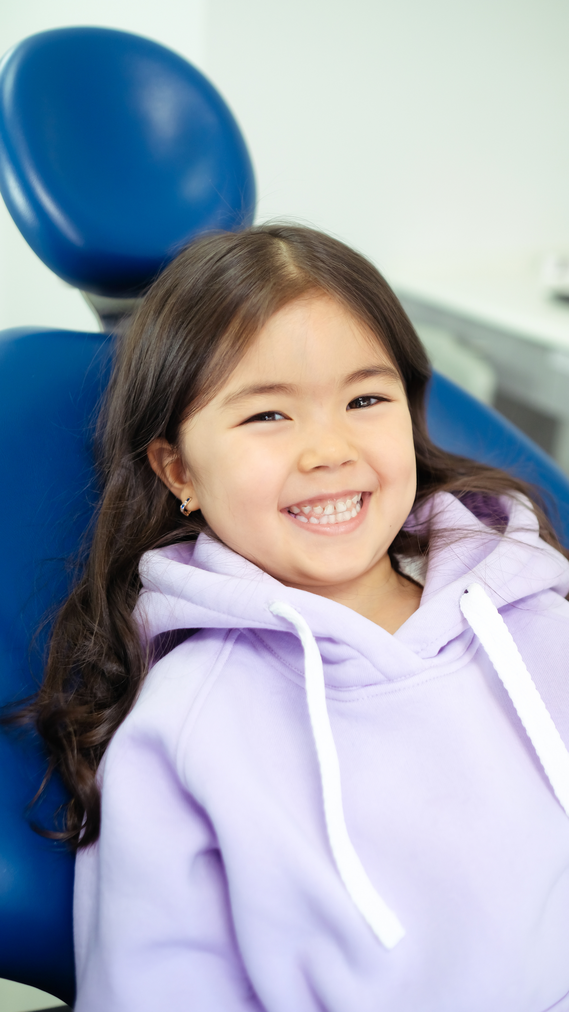 A little girl is sitting in a dental chair and smiling.