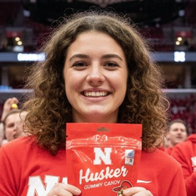 Woman smiling broadly in a green and white patterned shirt, standing in front of a white door.