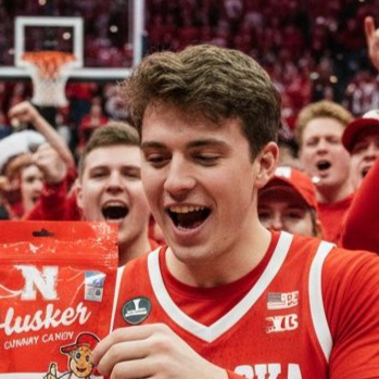 Man with curly hair smiles broadly against a dark, leafy background.