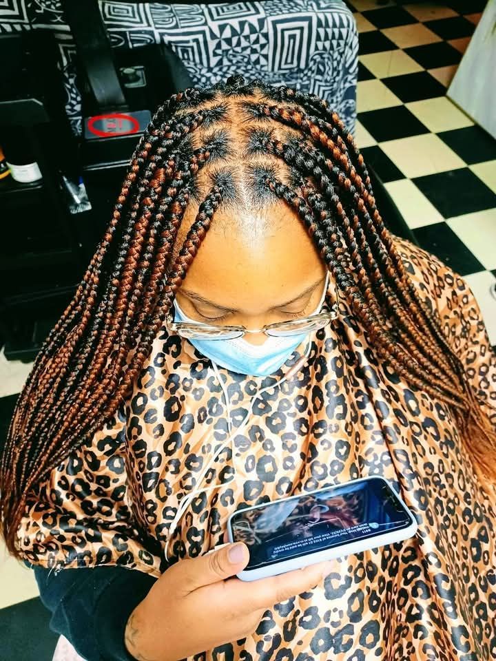 A woman with braids is wearing a mask and looking at her phone.