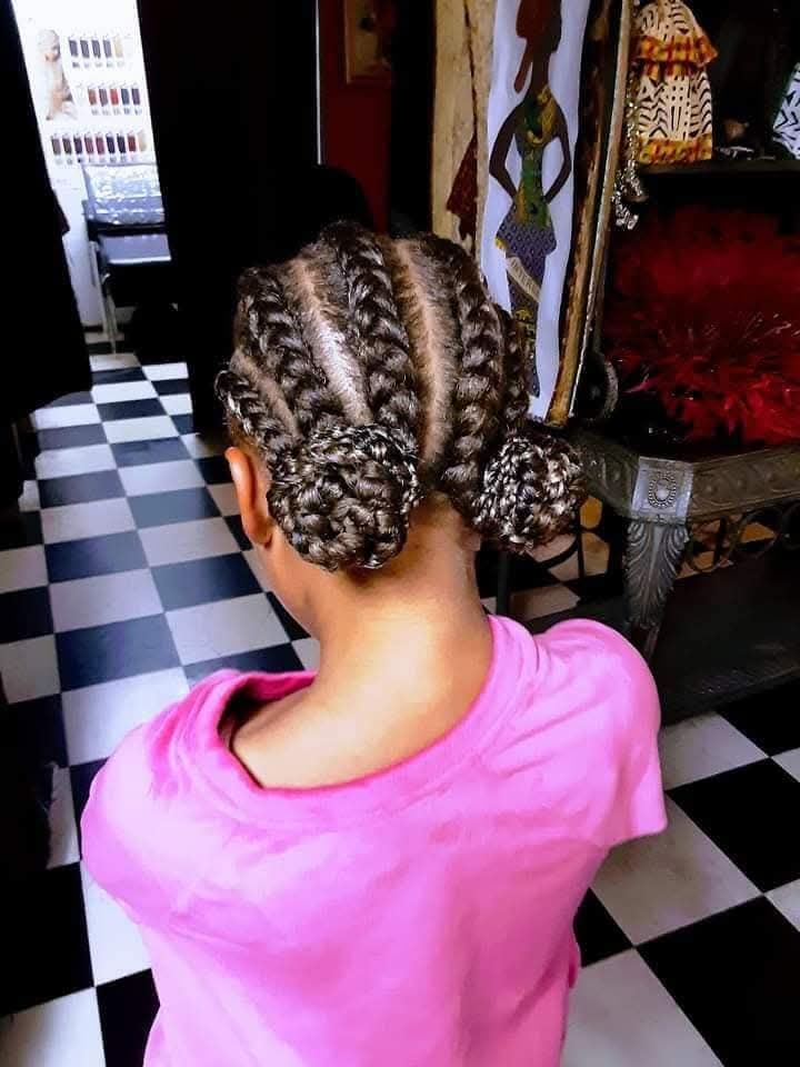 A little girl with braids in her hair is wearing a pink shirt