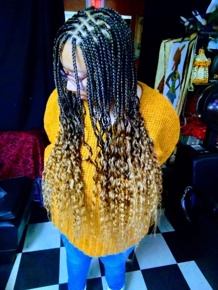 A woman with braids and curly hair is wearing a yellow sweater.