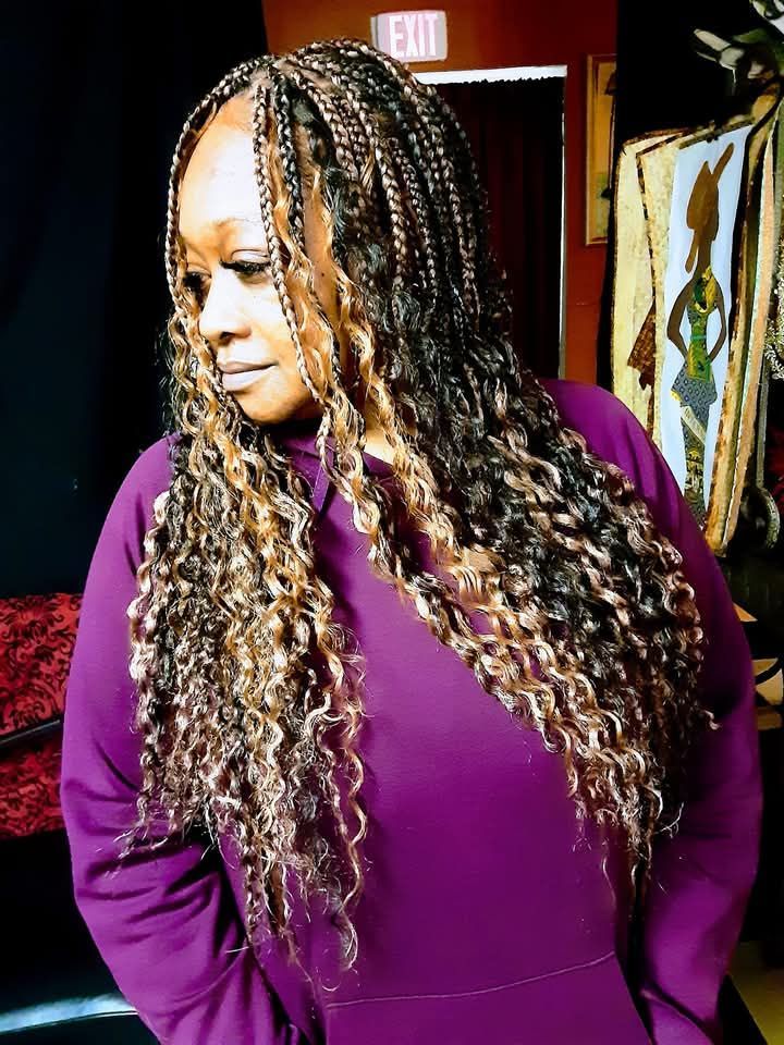 A woman with braids and curly hair is wearing a purple dress.