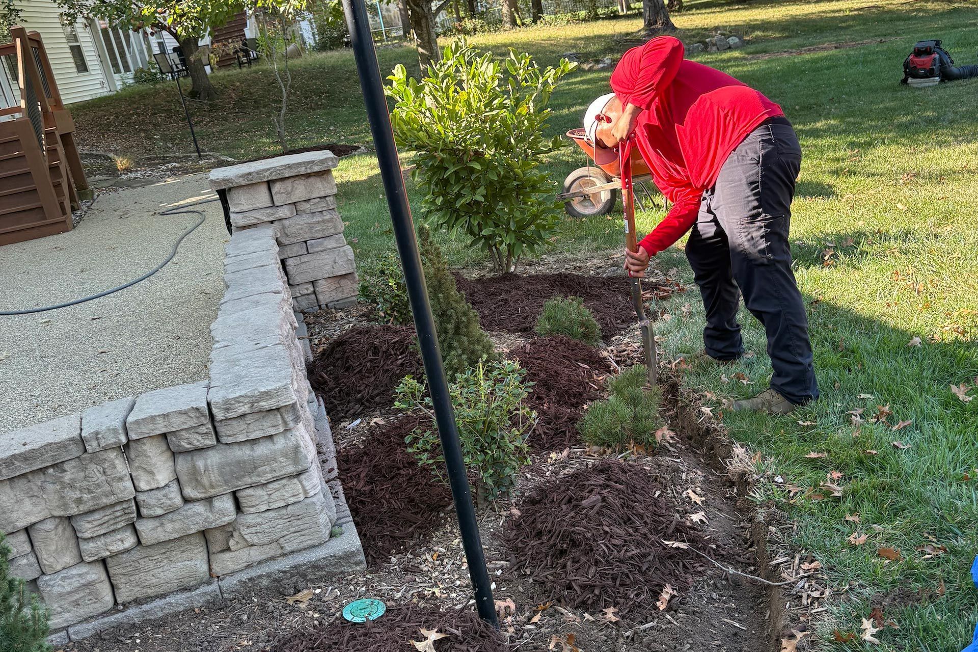 Person waters plants in a garden bed with mulch near a stone patio.