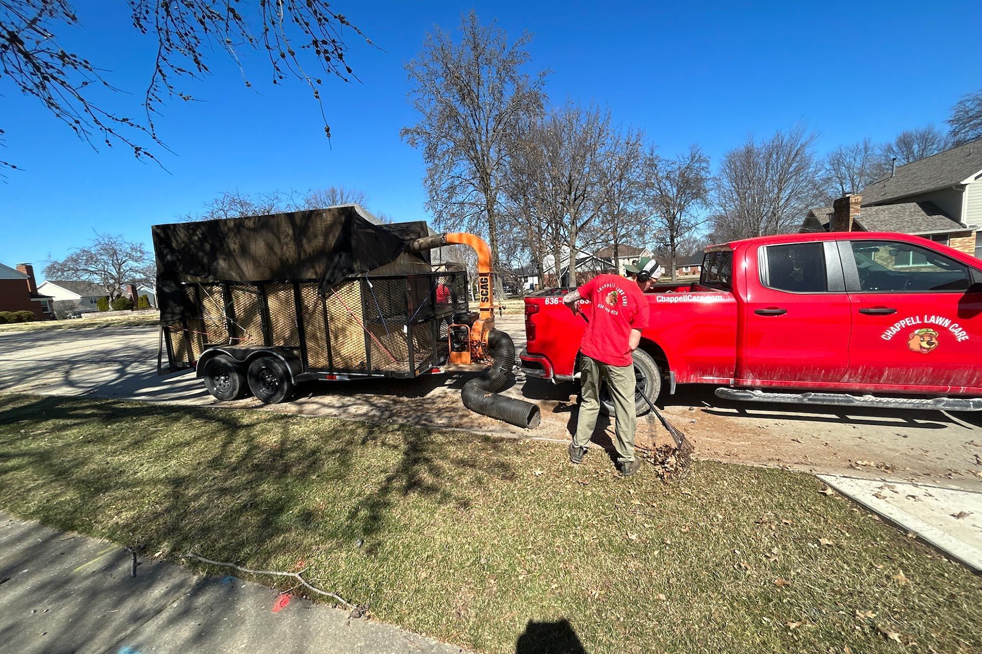 Person loading leaves from yard into trailer next to red truck. Sunny day.