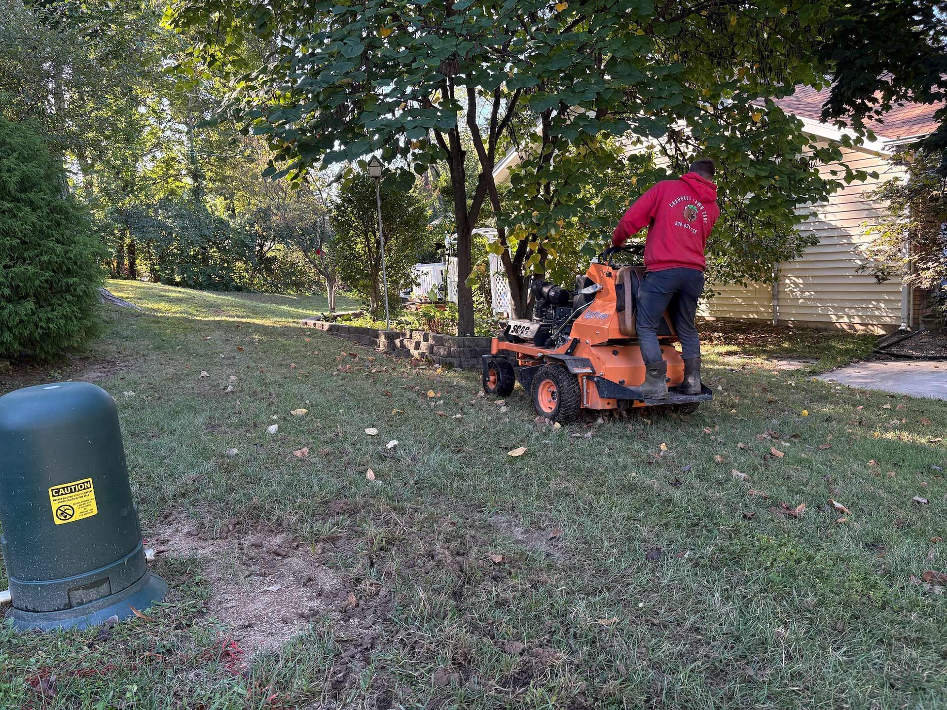Man in red sweatshirt using a riding mower on a grassy hill.