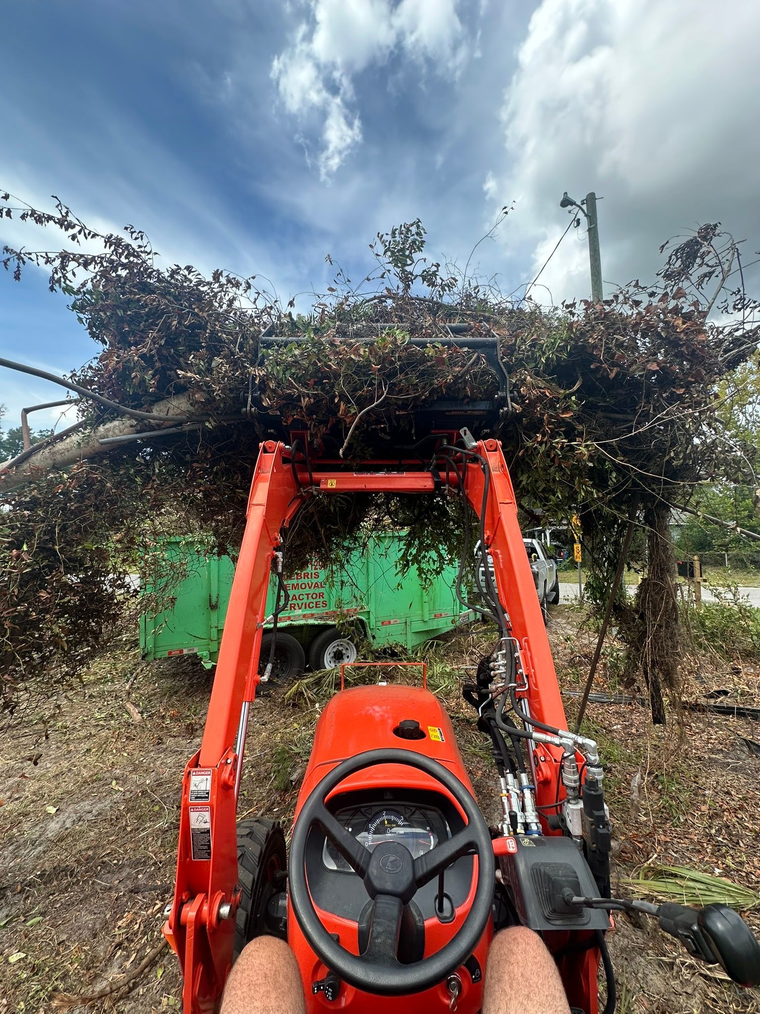 A person is driving a tractor with a large pile of branches on the back.