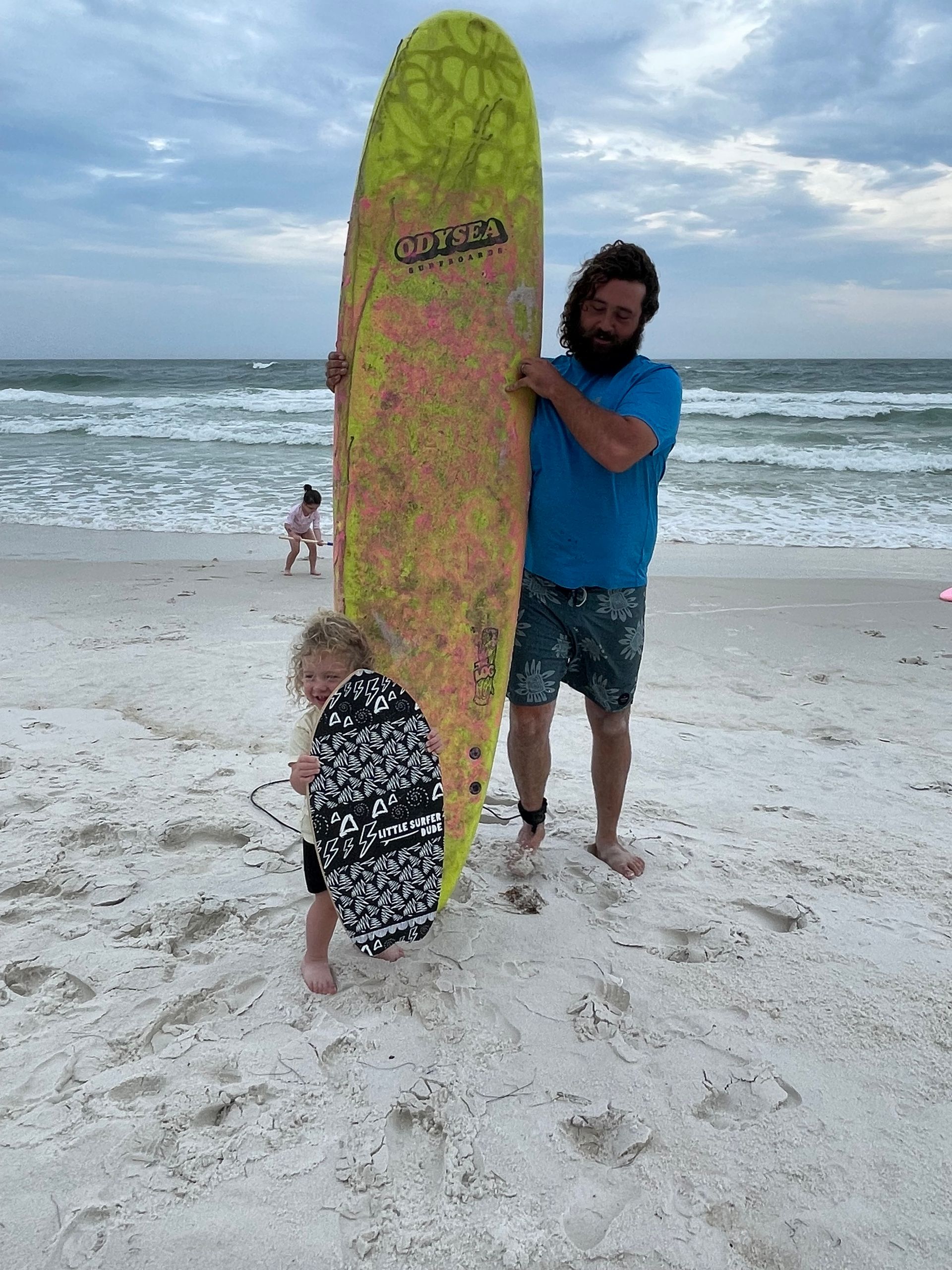 A man and a child are holding a surfboard on the beach.