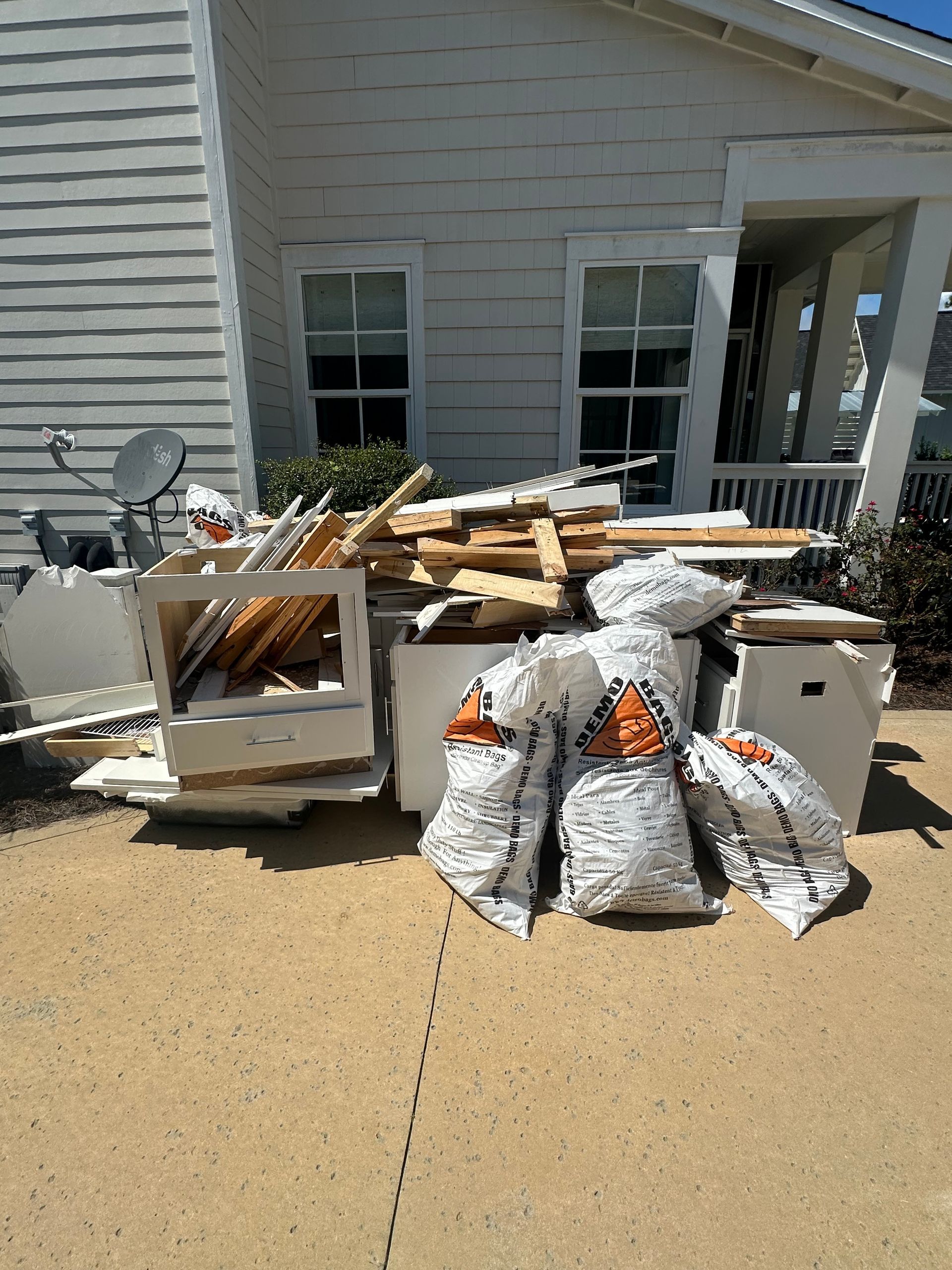 A pile of trash is sitting on the sidewalk in front of a white house.