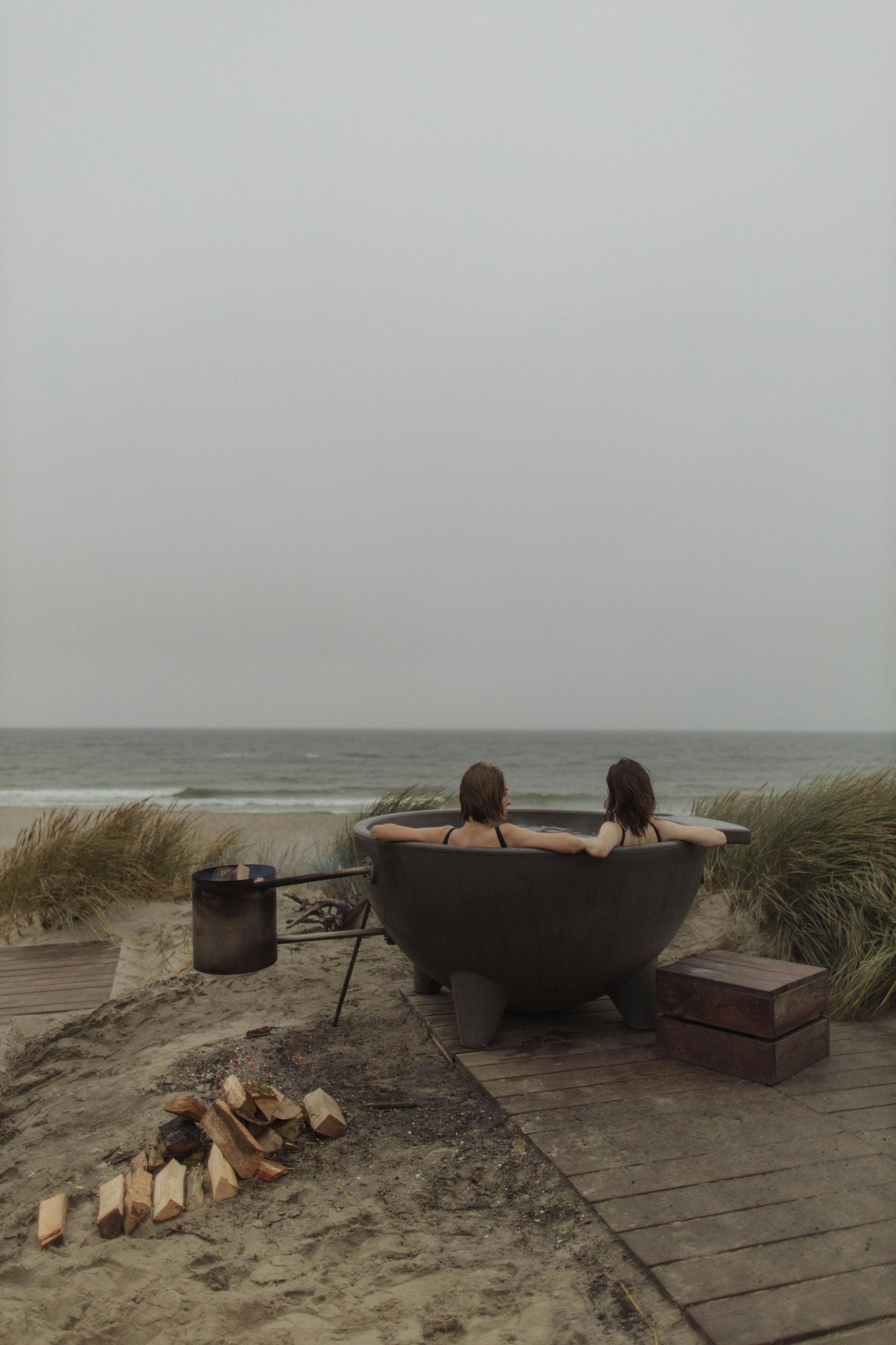 Two people are sitting in a hot tub on the beach.