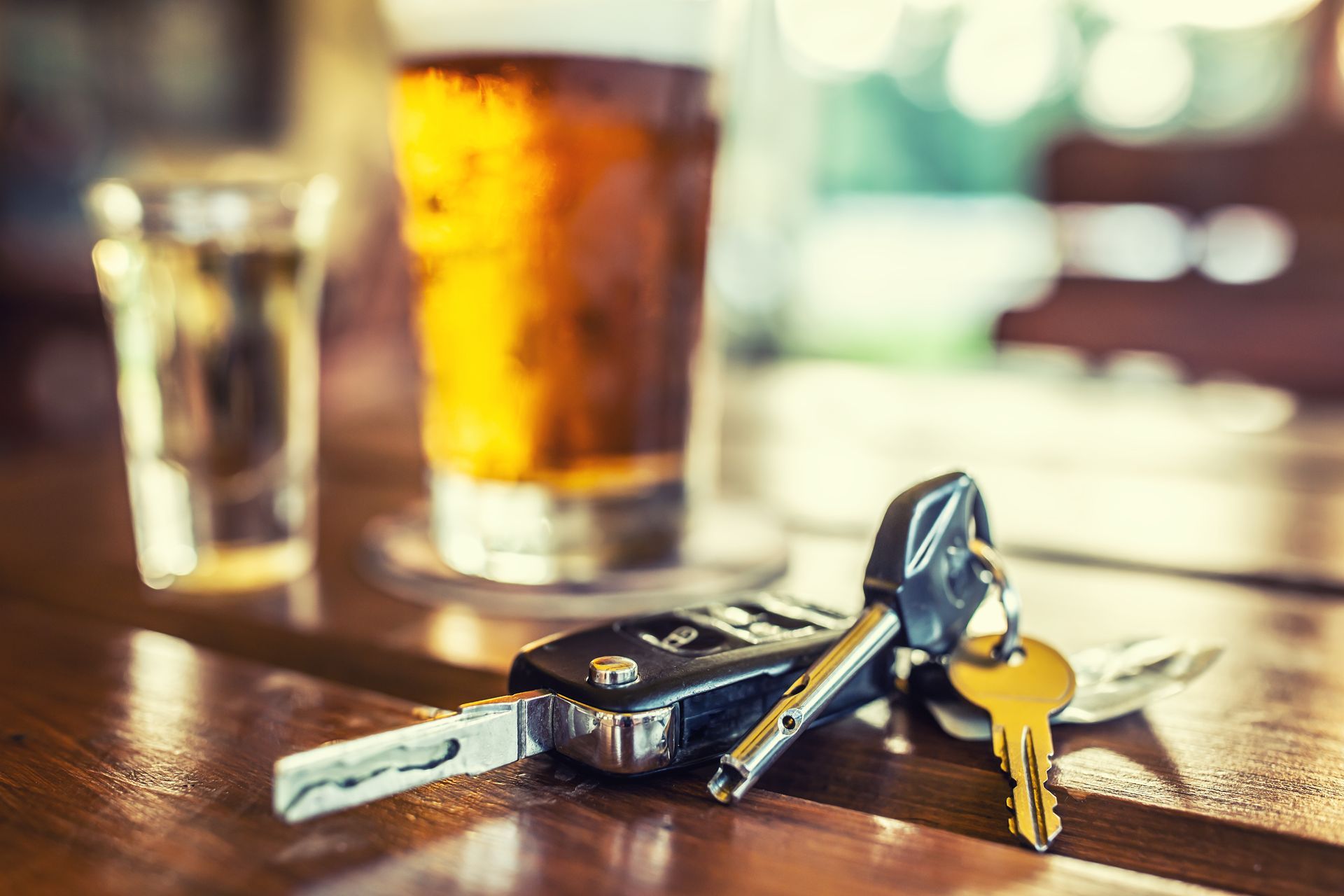 A car key is sitting on a bar counter next to a glass of beer.