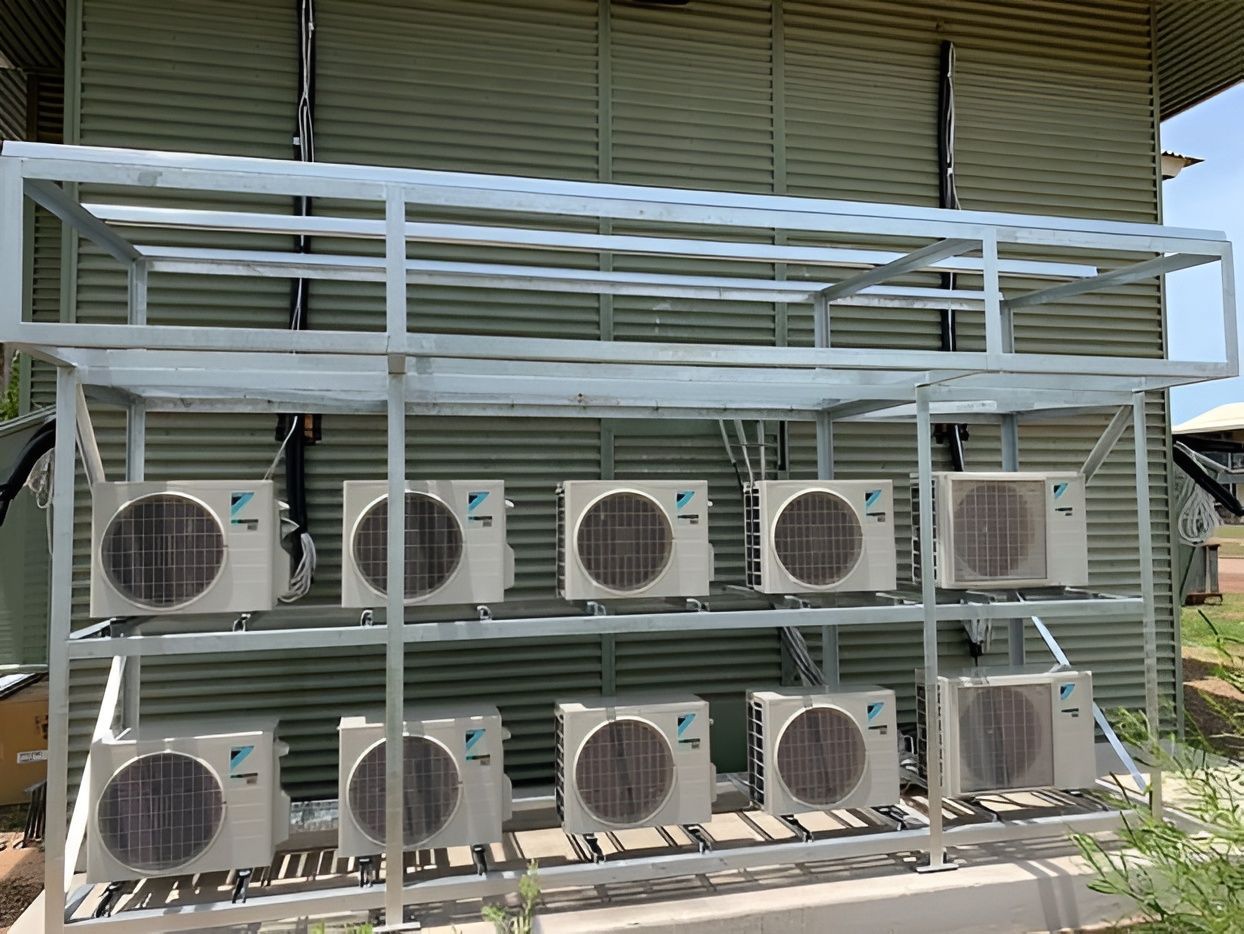 White metal rack holding many outdoor air conditioning units against a corrugated building. — Active Airconz in Darwin, NT