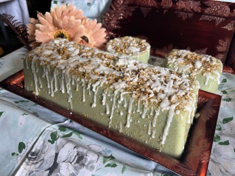 Green frosted cake, rectangular and round slices, drizzled with white icing and nuts, on a tray.
