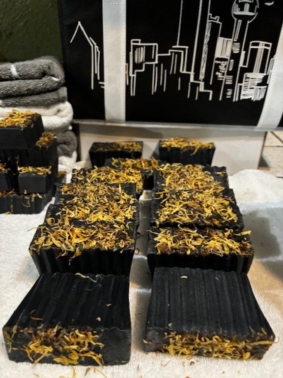 Rows of dark rectangular soaps, topped with yellow flower petals, arranged on a white surface.