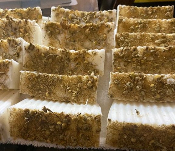 Rows of rectangular bars of soap with dried herbs on top.