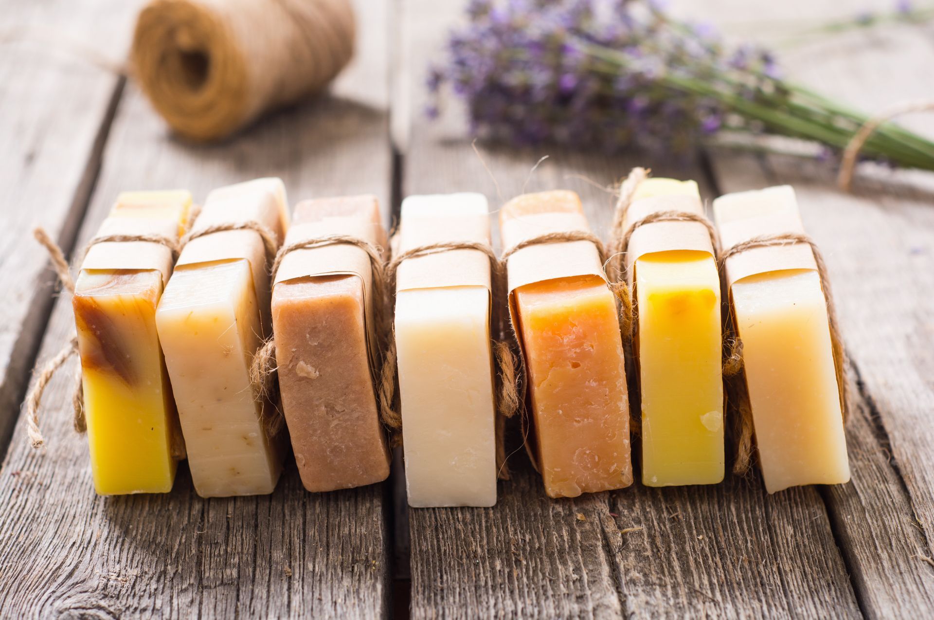 Bars of handmade soap tied with twine on a weathered wooden surface, with lavender in the background.
