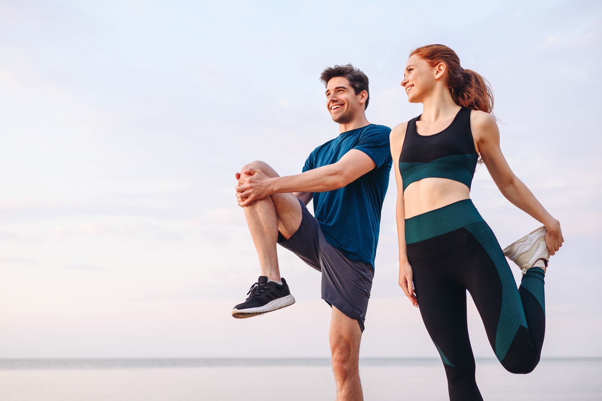 Man and woman stretching outdoors, sky and water background.