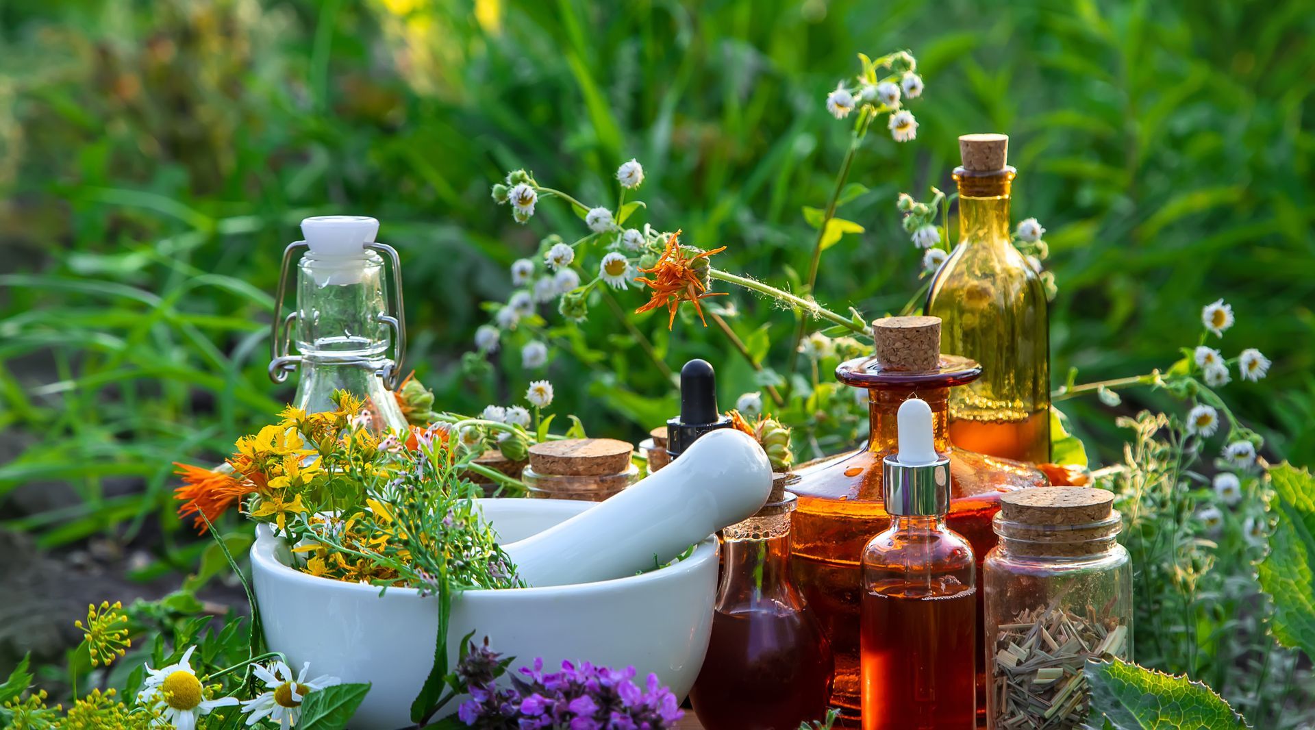 Herbs and oils with mortar and pestle in garden setting.