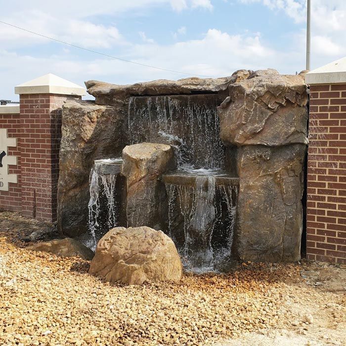 A Waterfall Is Surrounded by Rocks and A Brick Wall