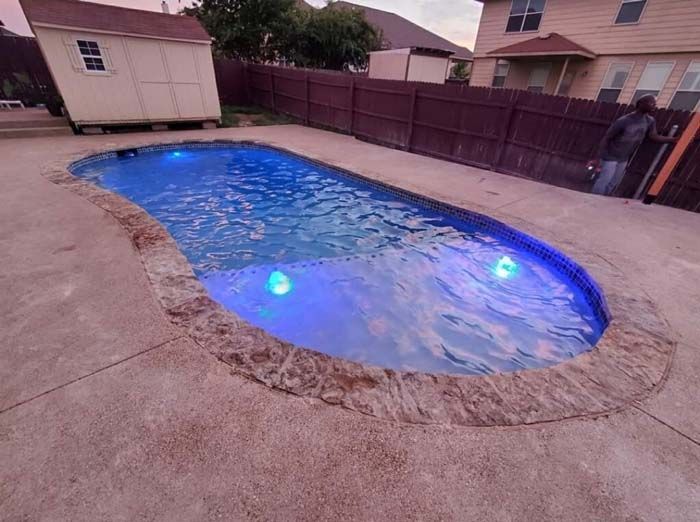 A Large Swimming Pool Is Lit up With Blue Lights in A Backyard