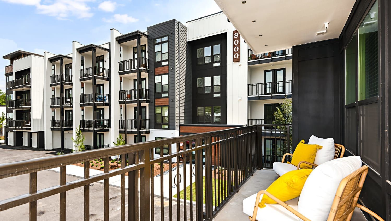 Balcony with wicker chairs and yellow cushions on a modern apartment building exterior.