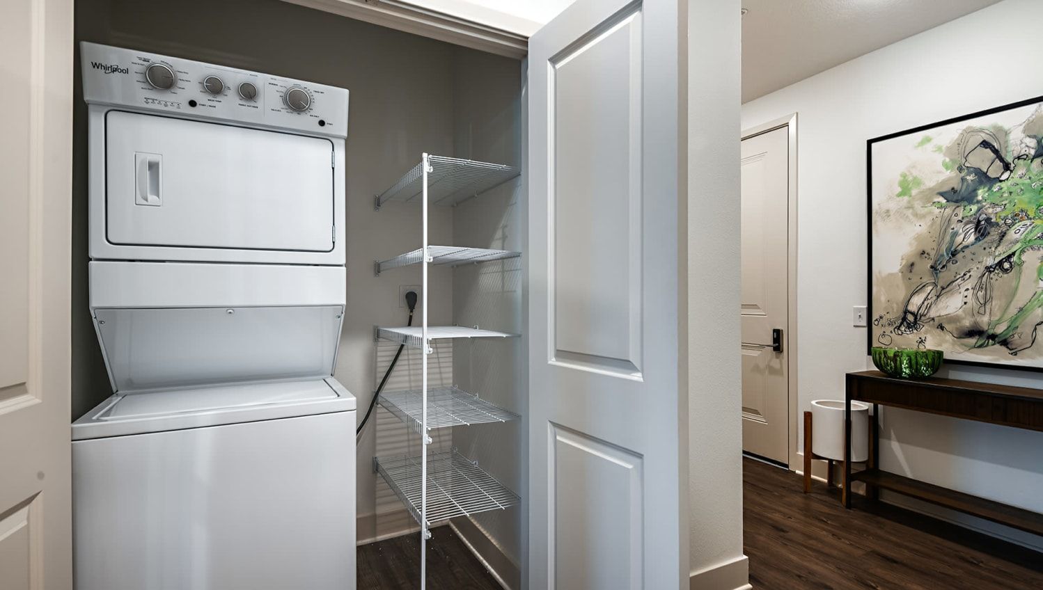 In-unit stacked washer and dryer in a small closet with metal wire shelves.