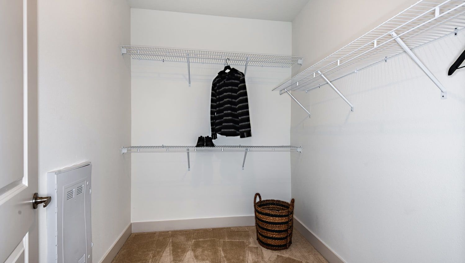 Walk-in closet with white walls, wire shelving, a striped jacket, and a wicker basket.