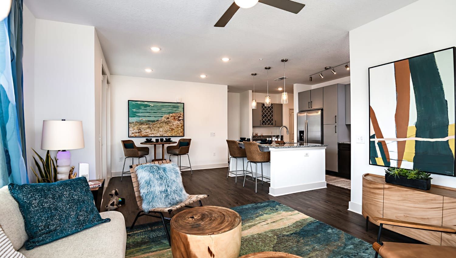 Open-concept living room and kitchen in a modern apartment with seating, rug, and artwork.