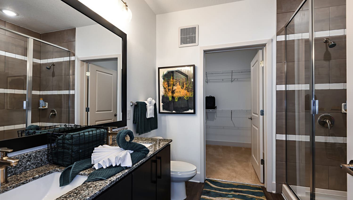 Bathroom with a granite double vanity, glass shower, and a walk-in closet in the background.