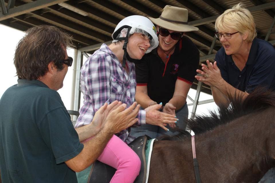 A person with a helmet on horseback is cheered on by three people.