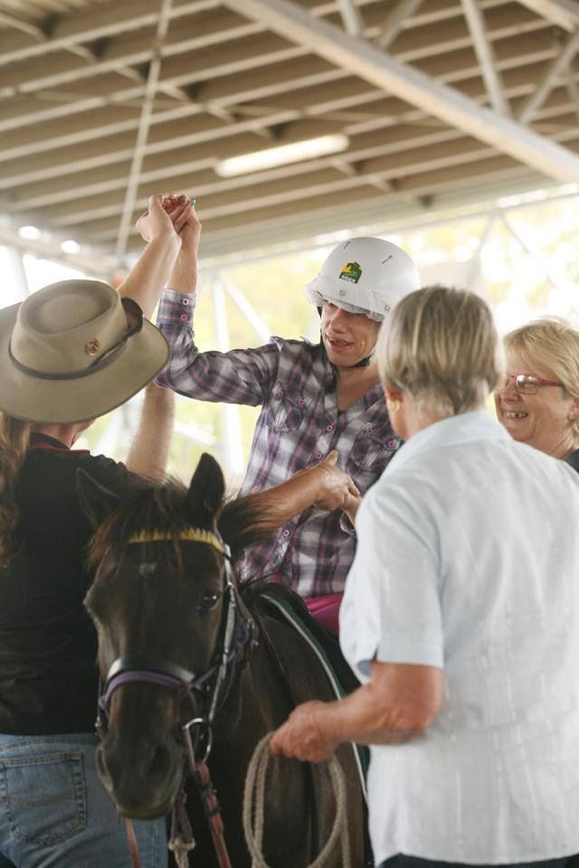 Person on a horse raises hand in celebration, surrounded by people, under a covered area.