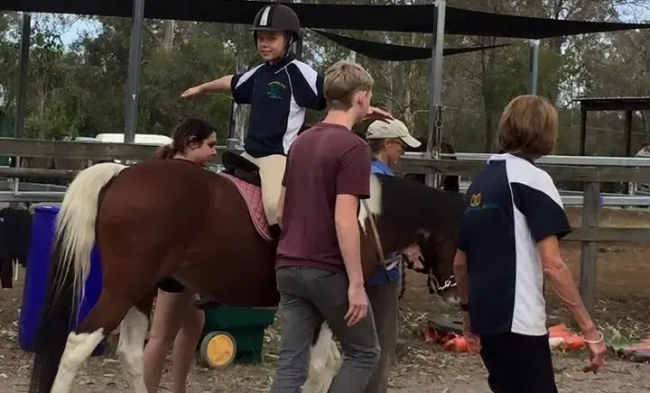 A child rides a horse with assistance from adults in an outdoor arena.