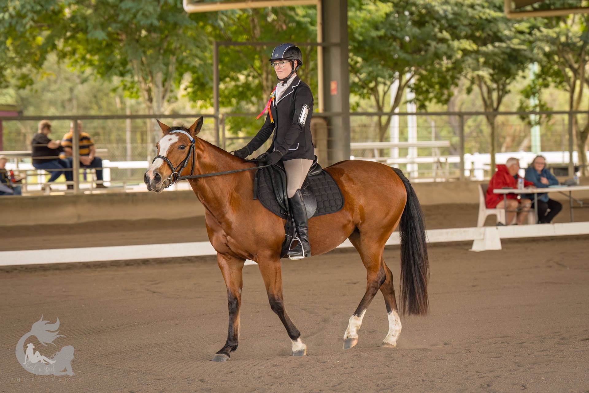 Woman on chestnut horse in riding competition. Indoors, dirt arena. Horse has white markings.
