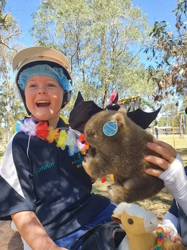 Child wearing a lei and hat smiles with a puppet.