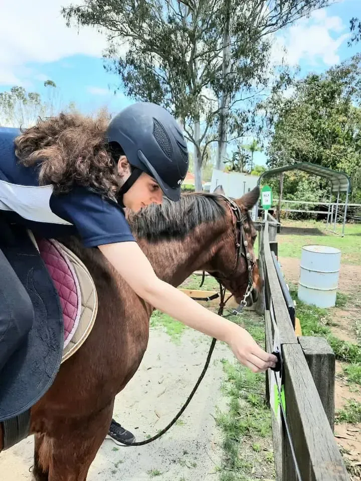 Person on horseback reaching toward a fence in an outdoor setting.