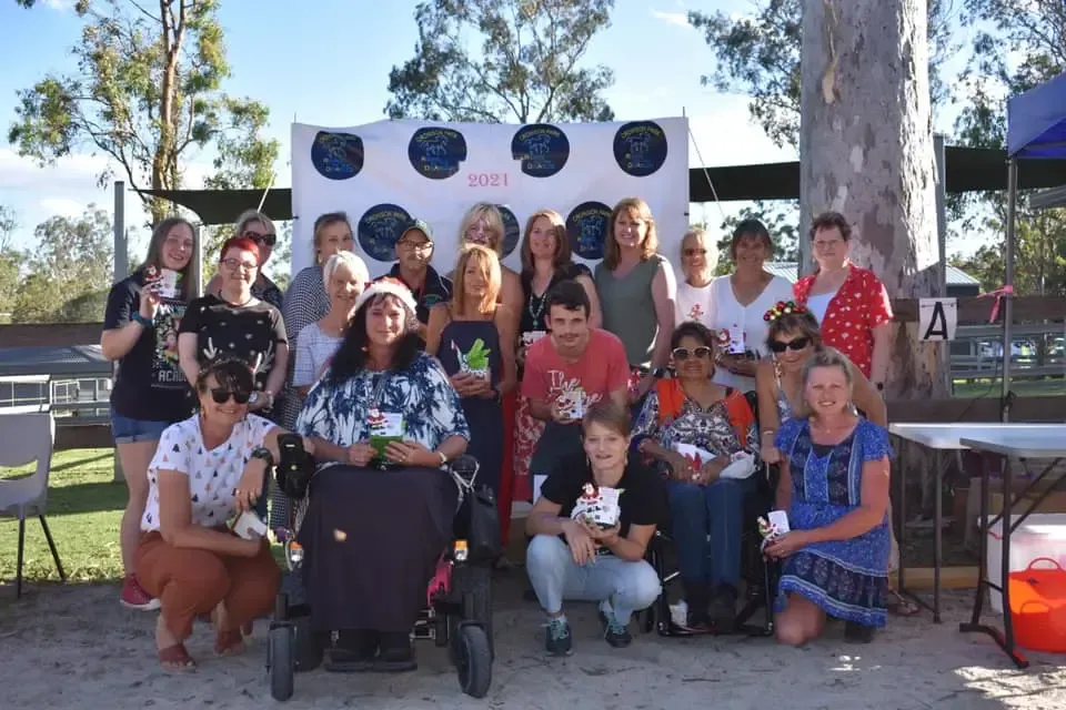 Group of people posing outdoors in front of a backdrop, some in wheelchairs, sunny day.