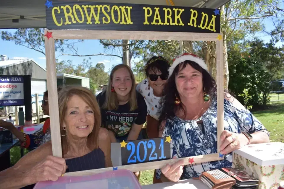 Group of people posing with a photo frame at a Crowson Park RDA event. Smiling, some wearing festive hats.
