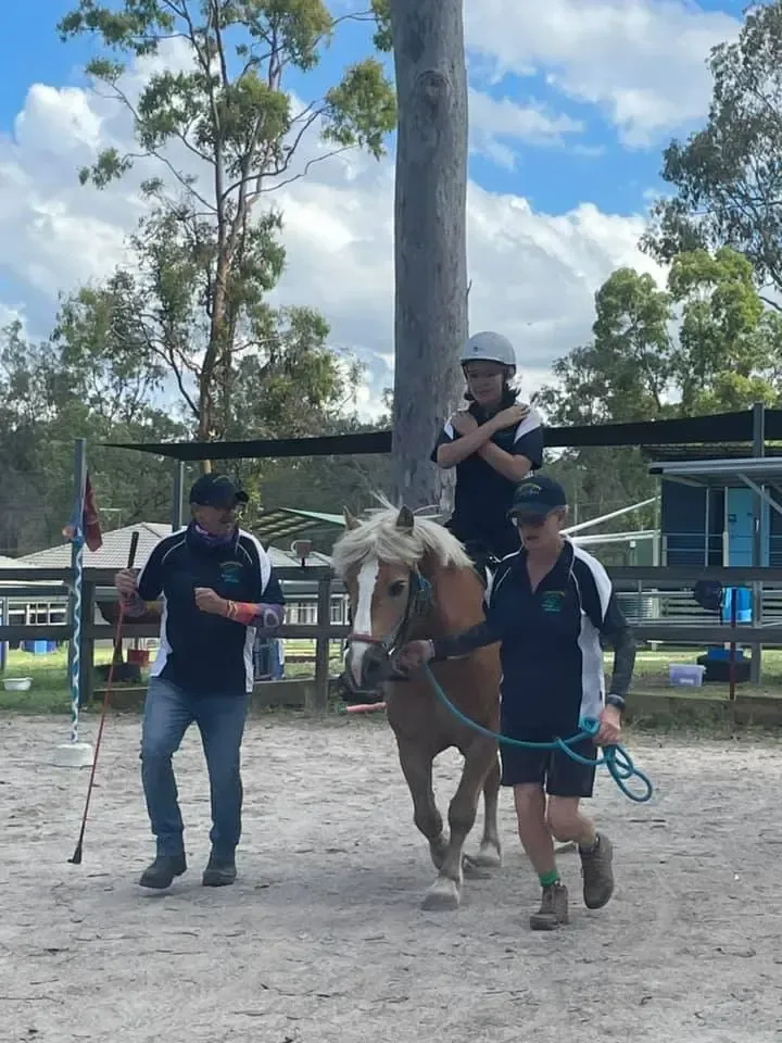 A person rides a pony led by two people in an outdoor arena.